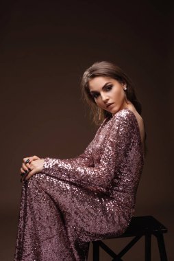 Stüdyoda zarif bir şekilde oturan pırıl pırıl pembe pullu elbiseli zarif bir kadın. Moda modeli pozu