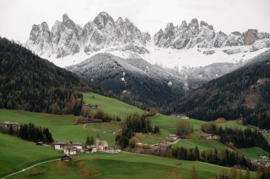 Kilisesi ve dağınık evleri olan pitoresk bir köy, koyu çam ormanları ve dramatik, karla kaplı dağlarla çevrili yuvarlak yeşil otlaklarda huzur içinde oturuyor.