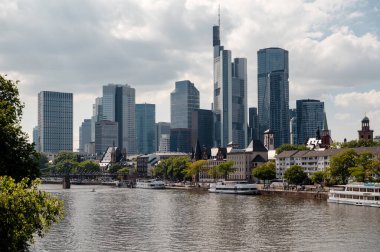 Frankfurt 'un finans bölgesinin panoramik manzarasında, akan ana nehrin yanında çağdaş yüksek binalar ve tarihi mimarinin bir karışımı sergileniyor.