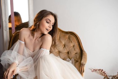 Güzel bir gelin ya da manken lüks bir antika sandalyede zarifçe poz verir. Omuzdan düşme elbisesi romantik bir siluet yaratır.