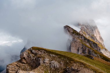 Seceda 'nın dramatik, pürüzlü zirveleri, heybetli bulutların arasından yükseliyor, İtalyan Dolomitlerin dağ sırasının engebeli güzelliğini sergiliyor.