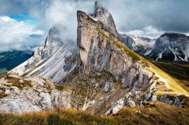 İtalyan Dolomitleri 'nde Seceda' nın sarp tepelerinde dramatik bulutlar kıvrılır, dağlık arazide dolambaçlı bir yürüyüş yolunu vurgular.