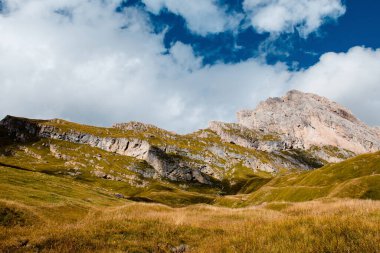 İtalyan Dolomitlerindeki Seceda tepelerinin geniş bir görüntüsü, engebeli tepeler, çimenli yamaçlar ve dağınık bulutlu dinamik bir gökyüzü.
