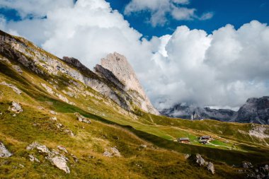 Dramatik bulutlar, İtalya 'nın Dolomitlerin yeşil dağlık çayırlarına kurulmuş ikonik Seceda dağ sırtları ve geleneksel ahşap kulübelerin üzerinde toplanıyor.