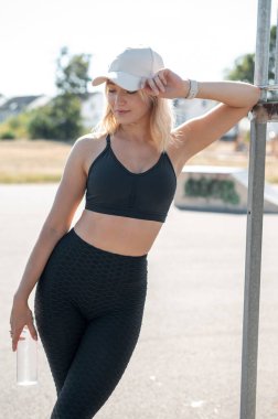 Sporcu genç bir kadın güneşli bir açık hava kaykay parkında dinlenirken biraz su içmek için mola veriyor.