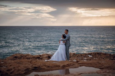 Gelin ve damat, gün batımında Akdeniz 'e bakan kayalık bir kıyı şeridini kucaklıyor.