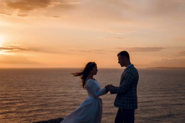 Gelin ve damat düğün günlerinde gün batımında denize bakan bir uçurumda el ele tutuşuyorlar.