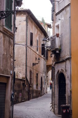 Dar bir kaldırım taşı caddesi, İtalya 'nın Tivoli kentindeki yıpranmış cepheleri ve geleneksel kepenkleri olan tarihi binaların arasından esiyor.