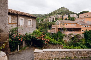 Tivoli, İtalya 'nın pitoresk bir manzarası, büyüleyici taş binalar, yemyeşil ve bulutlu bir gökyüzü altındaki uzak yamaçlar.