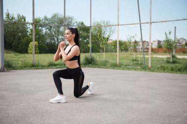 Siyah spor kıyafetleri içindeki atletik kadın, gündüz oturumunda güç ve denge ve sıcak hava antrenmanı koşullarına odaklanıyor.