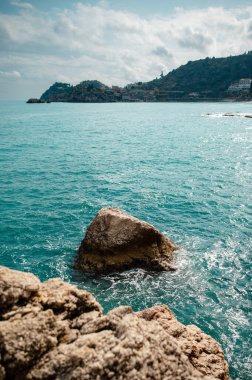Önünde yıpranmış kayalar olan canlı mavi denizi gören bir yamaçtaki kıyı kasabasının manzarası.