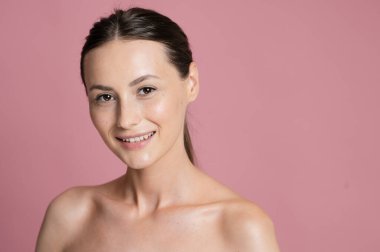 Temiz, parlak ciltli ve doğal bir gülüşü olan güzel bir kadın, sağlıklı ten rengini ve pürüzsüz deri dokusunu vurgulayarak kendine güvenle poz verir.