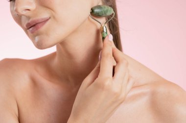 Bir kadının yüzüne ve omzuna yakın çekim yaparken yanağına doğal taş bir yüz silgisiyle nazikçe masaj yapıyor.