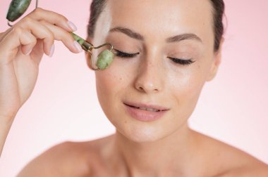 Bir kadın yeşil yeşim bir yüz kaydırma aletiyle nazikçe göz altına masaj yapıyor.