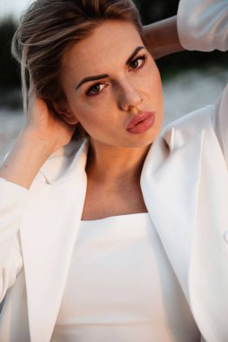 Doğal makyajı ve çilleri olan, elleri saçlarında, kendine güveni ve tarzı olan güzel bir kadının yakın plan portresi.