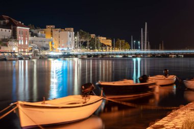 Hırvatistan 'ın Omis kentindeki sakin gece sahnesini, demirli tekneler ve aydınlık binalarla uzun süre gösteren sahne, sakin deniz yüzeyini yansıtıyor.