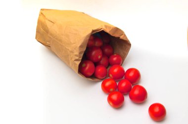 Parlak kırmızı kiraz domatesleri kahverengi bir kesekağıdından beyaz bir yüzeye dökülür. Çekim, çevre dostu paketlemeyi, organik üretimin tazeliğini ve hareketi vurguluyor. Ayrı nesne.