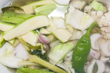 Çeşitli sebzelerin yakın çekimi: kabak, karnabahar, soğan, sarımsak ve tamamen salamura edilmiş yeşil biber. Mühürlemeye hazır bir turşu hazırlığı..