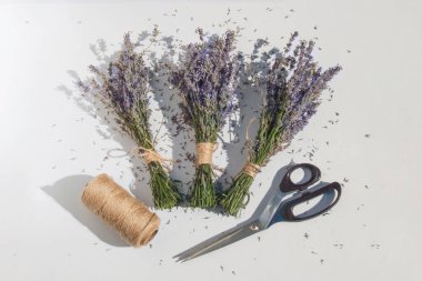 Çiçek işleminin son bileşimi. Üç estetik lavanta buketi, metal makas ve hafif bir yüzey üzerinde jüt. Bitmiş iş, tarım ürünü ve eko-dekor kavramı.