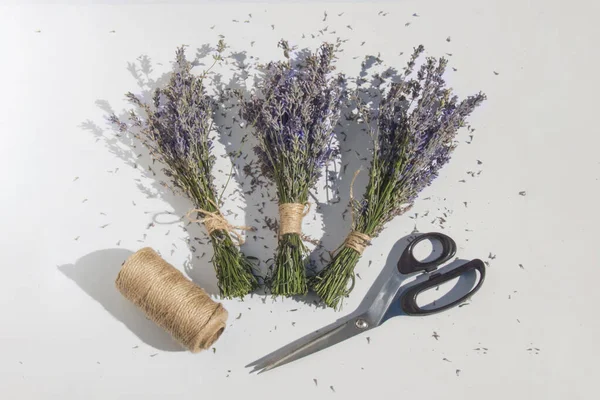 Çiçek işleminin son bileşimi. Üç estetik lavanta buketi, metal makas ve hafif bir yüzey üzerinde jüt. Bitmiş iş, tarım ürünü ve eko-dekor kavramı.