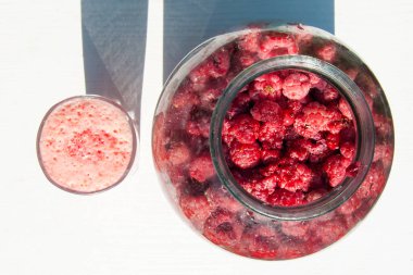 Makro üst manzara: olgun ahududu ve pembe köpüklü içecek. Parlak ışık, beyaz arka plan, canlı doğal fotoğraf. Vitamin, sağlıklı beslenme ve yaz hasadı kavramı.