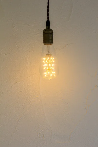 Žárovka visí na bílé zdi — Stock fotografie