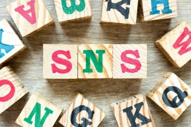 Kelime SNS ile alfabe harf bloğu (sosyal ağ sitesinin kısaltılmışı veya üzgün olmamak) ve ahşap arka planda başka bir sözcük.