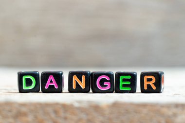 Ahşap arka planda kelime tehlikesi içeren siyah boncuk.