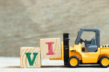 Tahta zemin üzerinde VI (değer yatırımcısının kısaltması) sözcüğünü tamamlamak için oyuncak forklift tutucu harf bloğu