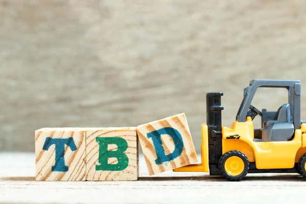 Toy forklift hold letter block d to complete word TBD (Abbreviation of to be defined, discussed, determined, decided, deleted or declared) on wood background