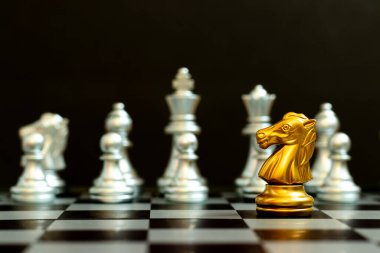 Satranç oyununda altın şövalye, siyah zemin üzerinde başka bir gümüş takım ile karşı karşıya (Şirket stratejisi, iş zaferi veya karar kavramı)