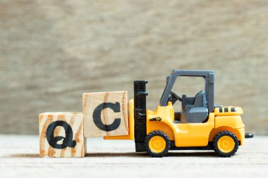 Tahta arkaplan üzerinde QC (Kalite Kontrolünün kısaltması) sözcüğünü tamamlamak için C harfi forklift engeli