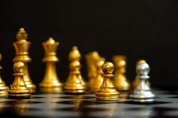 Silver pawn in chess game face with the another gold team on black background (Concept for company strategy, business victory or decision)