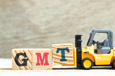 Oyuncak forklift harf bloğu T 'yi tahta arkaplan üzerinde GMT (Greenwich Ortalama Saatinin kısaltması) tamamlamak için tut
