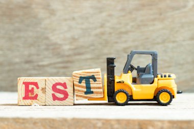 Oyuncak forklift, ahşap arkaplan üzerinde kurulu, tahmini, doğu zaman diliminin kısaltması olan EST sözcüğünü tamamlamak için t harfi bloğunu tutar.