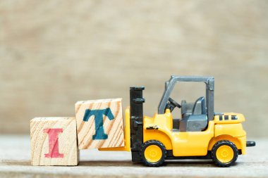 Oyuncak forklift harf bloğu T 'yi ahşap arkaplan üzerine bilgi teknolojisinin kısaltması olarak tamamlamak için