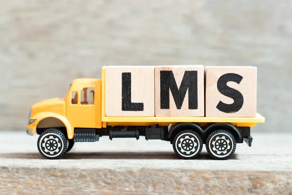 Toy truck hold alphabet letter block in word LMS (Abbreviation of Learning management system) on wood background