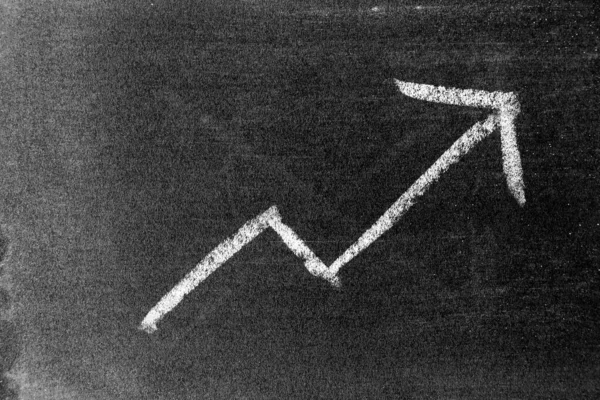 White chalk draw as upward arrow graph on blackboard or chalkboard background (Concept for sale, profit, cost of company in uptrend)