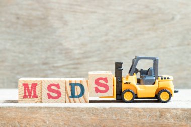 Oyuncak forklift, ahşap arkaplan üzerindeki MSDS (malzeme güvenlik veri tablosunun kısaltılması) sözcüğünü tamamlamak için S harfi blok bloğunu tutar