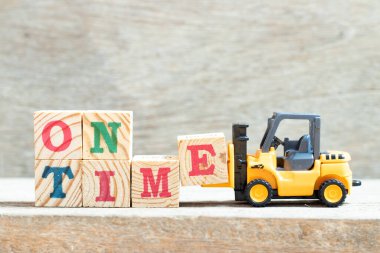 Oyuncak forklift harf bloğunu ahşap arkaplanda tam zamanında tut