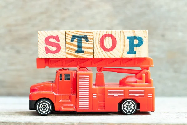 Fire ladder truck hold letter block in word stop on wood background