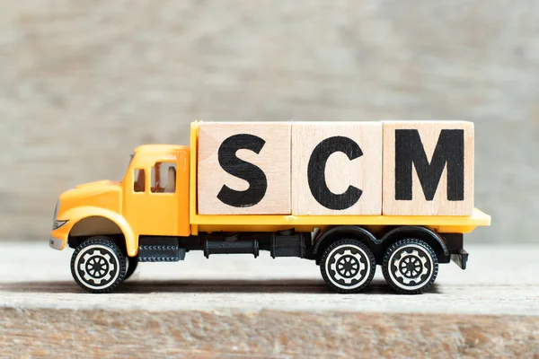 Toy truck hold alphabet letter block in word SCM (Abbreviation of Supply chain management) on wood background