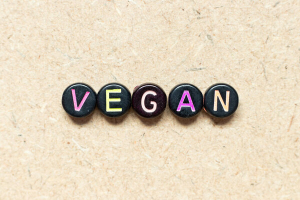 Black color round bead in word vegan on wood background