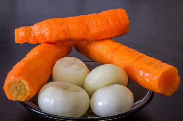 Assiette en verre sur table noire avec les oignons rouges crus purifiés et les carottes cuisiner — Photo