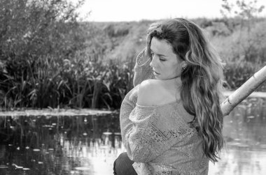 Genç güzel kadın modeli uzun sarı saçlı oturan farklı duygular kahkaha, üzüntü, keder, dalgınlık Nehri ve su almak için ormanın kıyısında ahşap bir köprü ile