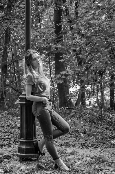 Joven hermosa chica sexy modelo rubio con pelo largo y rubio en jeans y chaqueta posando en el bosque entre los árboles y la vegetación —  Fotos de Stock