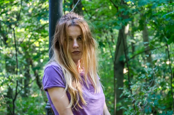 Jonge mooie sexy meisje blond model met lang blond haar in jeans en jas poseren in het bos tussen de bomen en vegetatie — Stockfoto