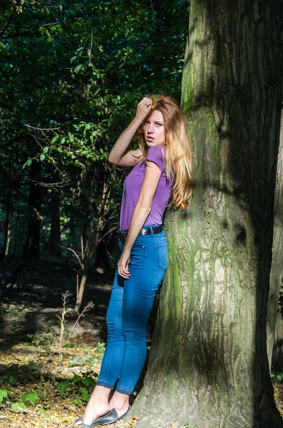 Молодая красивая сексуальная блондинка блондинка модель с длинными светлыми волосами в джинсах и куртке позирует в лесу среди деревьев и растительности — стоковое фото