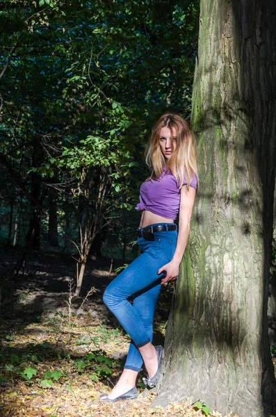 ジーンズとジャケットの森の木と植物中のポーズで長いブロンドの髪を持つ美しいセクシーな少女金髪モデル — ストック写真