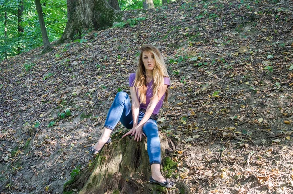 stock image Young beautiful sexy girl blond model with long blond hair in jeans and jacket posing in the woods among the trees and vegetation